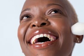 Smiling person with with makeup brush touching their cheek