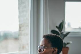 Person looking pensive while sitting at a desk holding a mug in front of their laptop