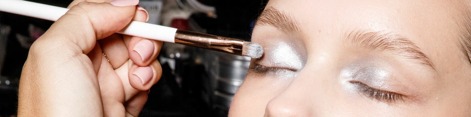 a model getting makeup done backstage at a fashion show