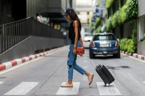 woman rolling a suitcase wearing jeans, a black tank top, and pink sneakers