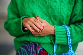 Ellie Delphine wears red nail polish with a green sweater.