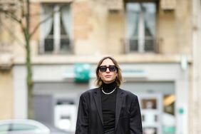 Person in a black body suit, blazer, and tights, with white socks and platform loafers