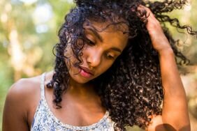 Model stands outdoors and looks down while running their hands through their hair.