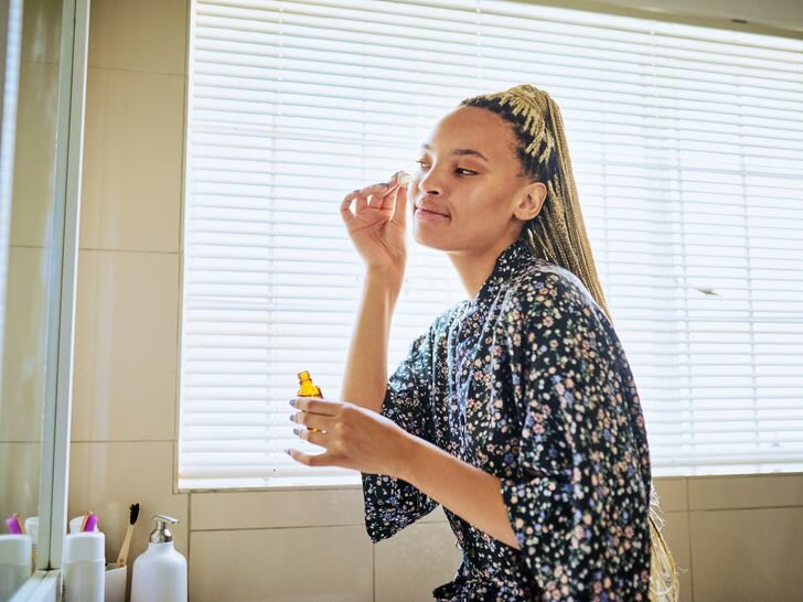 Young Black woman with long blonde braids applies facial oil